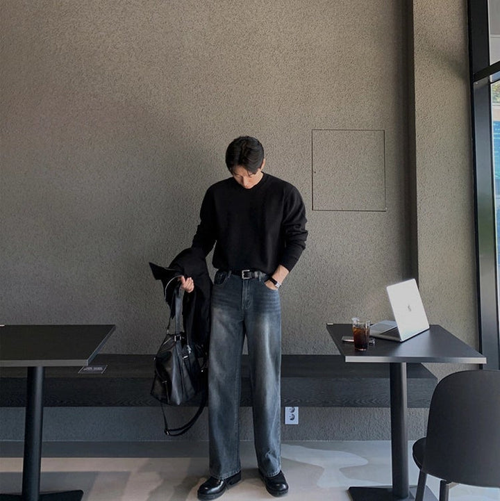 Person wearing gray jeans and black shoes in a minimal indoor setting.