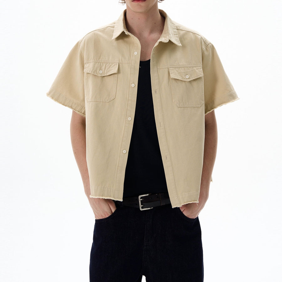 Person wearing a beige short-sleeve shirt over a black top on a white background